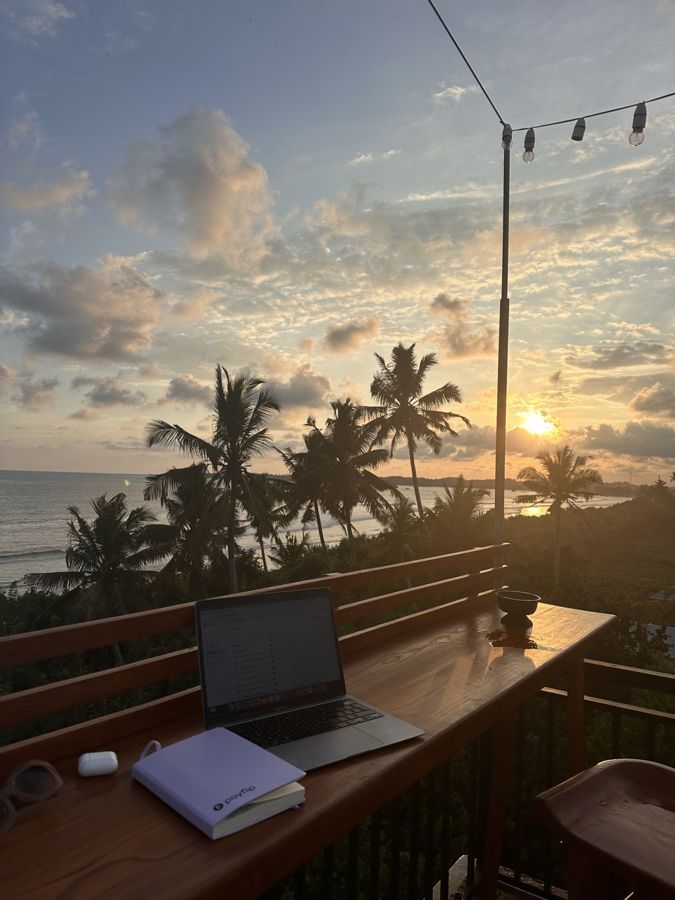 Laptop op een terras met palmbomen bij zonsondergang